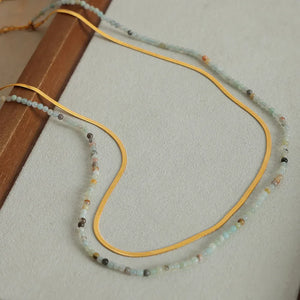 Gold serpentine chain layered with a delicate beaded necklace featuring pastel and earth-toned beads.