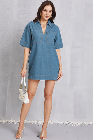 Denim mini dress with plunging collar, short sleeves, and two chest pockets in medium wash.