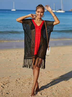Black crochet cover-up with red V-neck trim and fringe hem, worn on the beach.