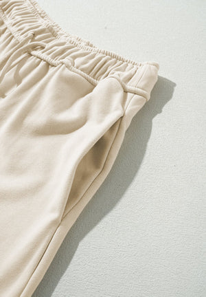 Beige wide-leg drawstring trousers with elastic waistband and side pocket detail.