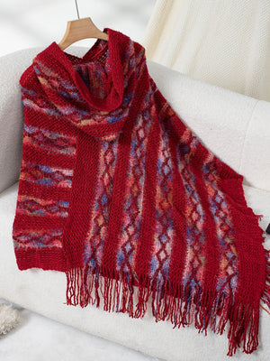 Textured knit hooded cape in red with diamond and stripe patterns and fringe detail.