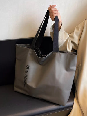 Grey minimalist large shoulder bag with black text detail and black straps.