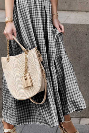 Black gingham maxi dress with smocked bodice and flutter sleeves, styled with a straw bag.