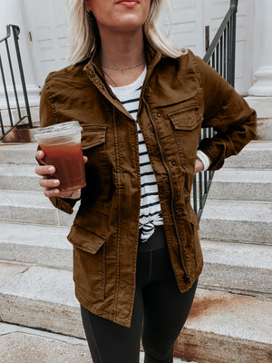 Brown utility jacket with multiple pockets, zip and button closure, styled casually.