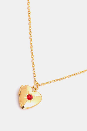 Gold heart locket necklace with red gemstone and starburst detail on a delicate chain.