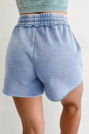 Blue cotton drawstring shorts with ruffled elastic waistband and raw hem.