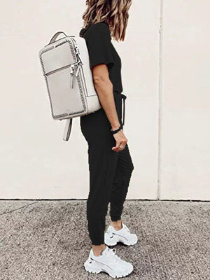 Black casual round neck top and jogger pants set with drawstring waist, styled with white sneakers and a backpack.