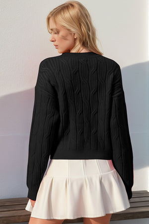 Black cable knit sweater with crew neck and long sleeves, styled with a white skirt.