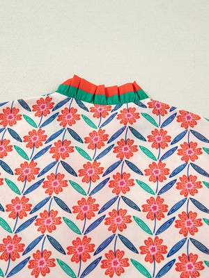 Floral ruffled v-neck shirt with orange and green striped trim and a colorful floral pattern.