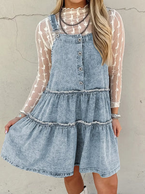 Tiered denim overall dress in light blue with button front and frayed hem tiers.