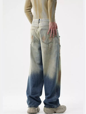 Men's distressed wide-leg jeans with a faded blue and tan ombre wash and brown stain details.