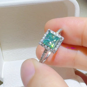 Radiant square halo moissanite ring in silver with a bright teal center stone and diamond accents.