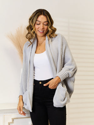 Light gray acrylic knit cocoon cardigan with pockets and open front, styled with a white tank and black jeans.