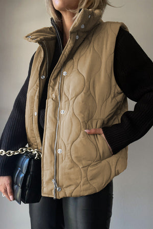 Quilted stand-collar gilet in taupe with zip and snap closure, styled with a black sweater and bag.