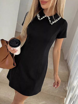 Black a-line mini dress with a beaded pearl collar and short sleeves.