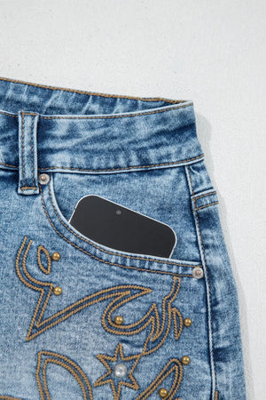 Light wash denim shorts with western embroidery, studs, and a phone in the pocket.