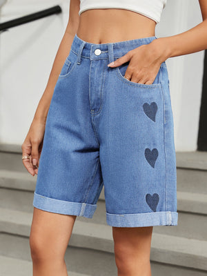 Medium wash denim bermuda shorts with dark heart appliqués and cuffed hems.