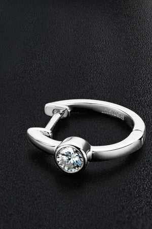 Silver huggie hoop earring with a bezel-set clear crystal on a black textured background.