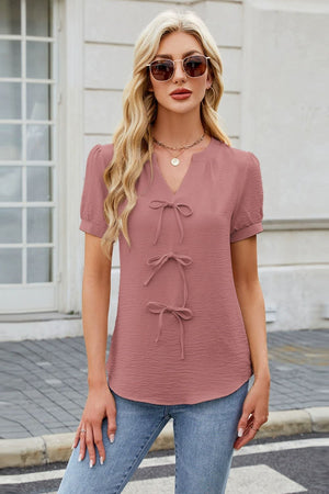 Dusty pink textured blouse with a V-neck and three bow-tie details.