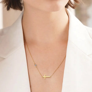 Gold asymmetrical cross pendant necklace with a single clear stone accent.