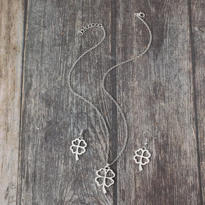 Silver four-leaf clover pendant necklace and matching earrings jewelry set on wood background.