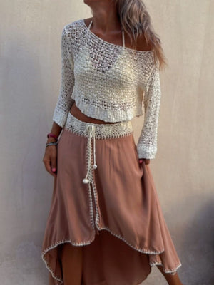 Asymmetric beige crochet crop top with long sleeves, styled with a high-waisted skirt.