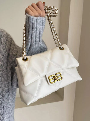 White quilted flap chain shoulder bag with gold hardware and a grey sweater.