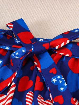 Patriotic baby outfit with red hearts, blue stars, and stripes pattern, featuring a bow detail.