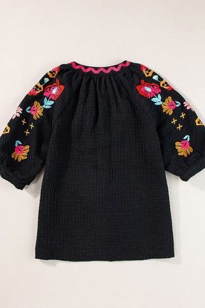 Black voluminous blouse with embroidered floral sleeves and pink scalloped neckline.
