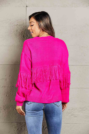 Hot pink acrylic cardigan with fringe detail on sleeves and back.