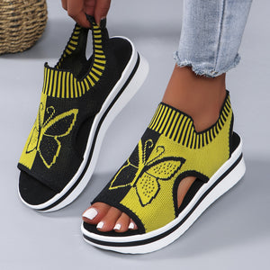 Yellow and black open-toe wedge sandals with butterfly motif and mesh detail.
