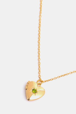 Gold heart locket necklace with green gemstone and starburst detail.
