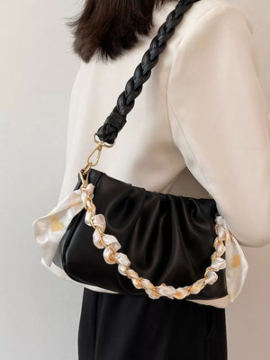 Black ruched shoulder bag with braided strap and decorative chain detail.