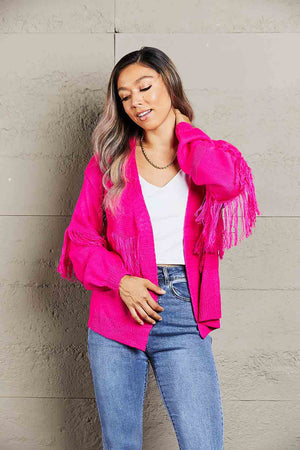 Hot Pink acrylic cardigan with fringe sleeves and open front, styled with jeans.
