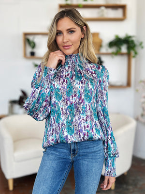 High neck abstract print blouse with smocked cuffs and neckline in blue, purple, and white.