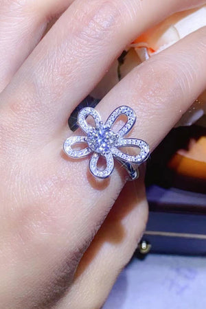 White moissanite flower ring with pavé details on a finger.