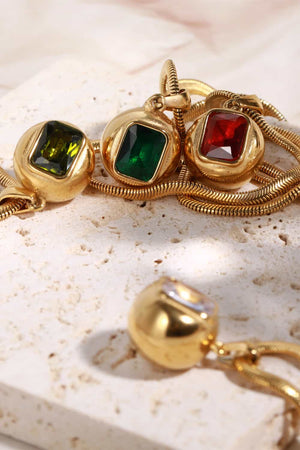 Gold necklace with orb and square pendants featuring olive, dark green, and deep red stones.