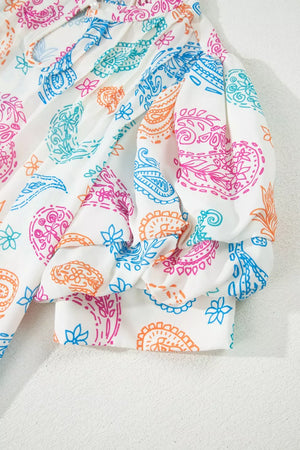 White maternity blouse with vibrant paisley print, puff sleeves, and frill detail.