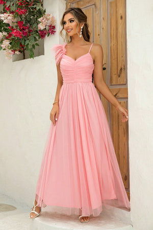 Blush pink tulle gown with sweetheart neckline, ruched bodice, spaghetti straps, and asymmetrical ruffle shoulder detail.