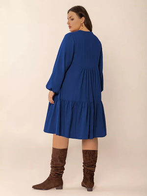 Plus-size dark blue A-line dress with tie-neck, button-front, and tiered skirt.