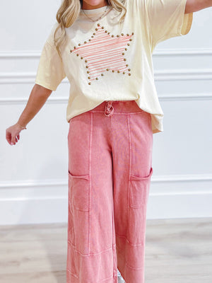 Cream t-shirt with pink striped star graphic and stud details, paired with pink wide-leg cargo pants.