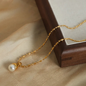 Gold pearl drop necklace with a delicate chain and oval bead accents.