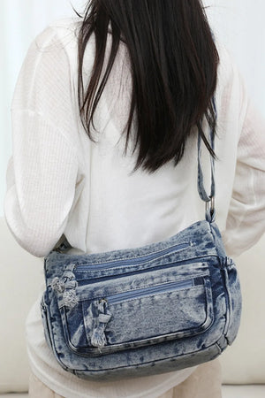 Acid wash denim crossbody bag with multiple zippered pockets and frayed details.