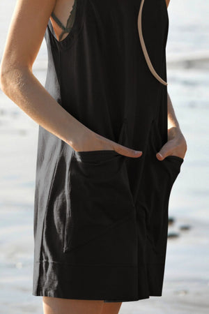 Black linen romper with pockets and relaxed fit, shown on model with hands in pockets.