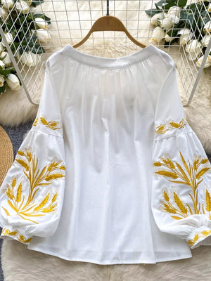 White embroidered tie-neck folk blouse with balloon sleeves and wheat detail.