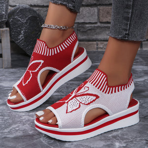 Red and white open-toe wedge sandals with butterfly motif mesh detail and chunky sole.