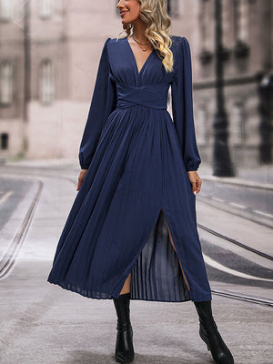 Dark blue pleated maxi dress with crossover waist, V-neck, long sleeves, and thigh-high slit.