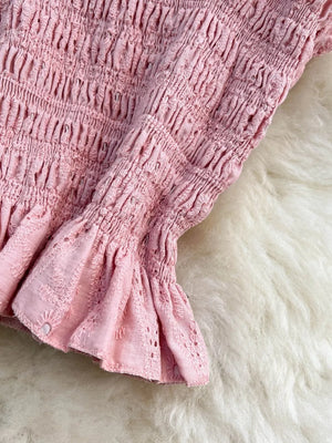 Pink ruffled crop top with eyelet detail and smocked sleeves.