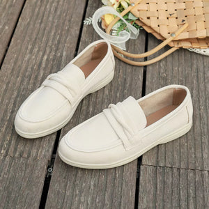Beige round toe slip-on loafers with decorative strap detail.