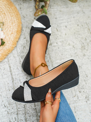 Black slip-on wedge flats with rhinestone bow detail.